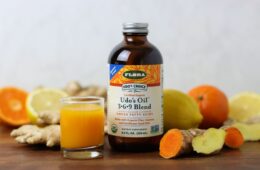A ginger turmeric wellness immune shot with a bottle of udos oil surrounded by ingredients
