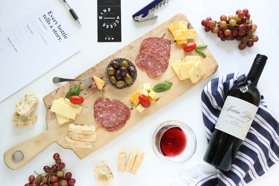 A bottle Martin Ray cabernet on a navy striped towel from Wine Access next to a cheese and meat board with olives and grapes