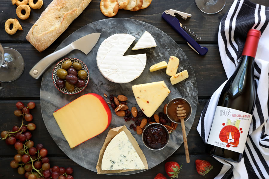 a round slate cheese board next to a bottle of Ciliegiolo Narni 05035